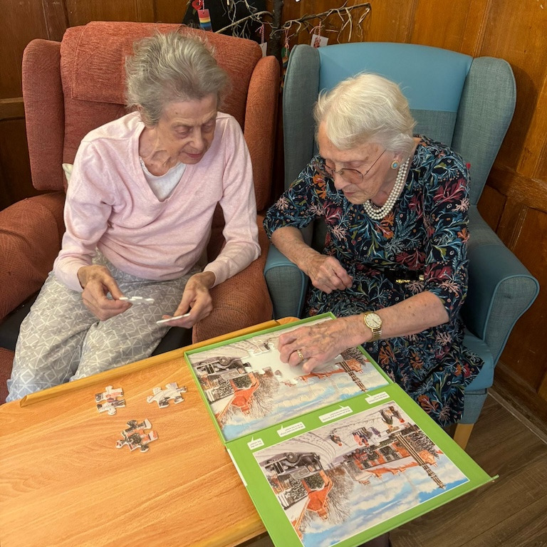 Two older women sat in armchairs doing a puzzle