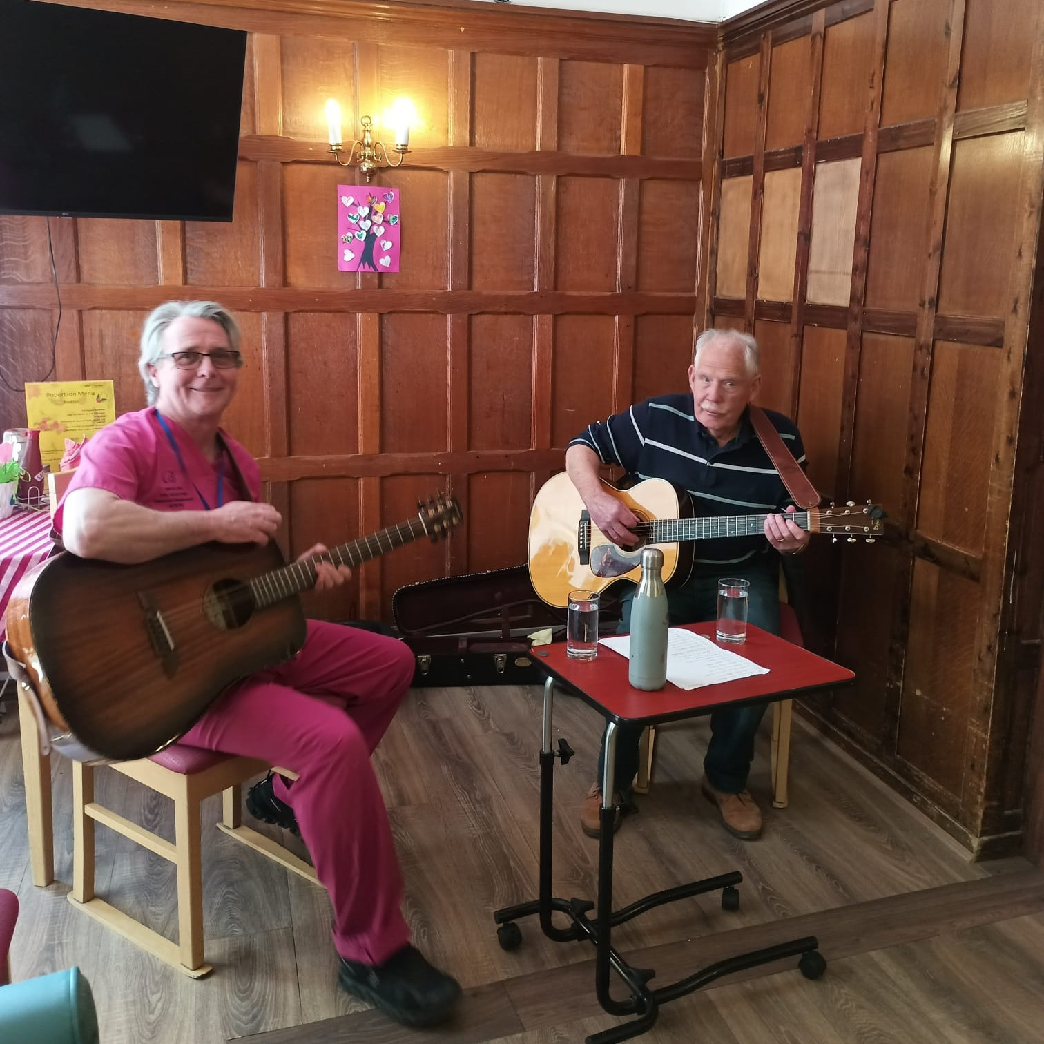 A staff member and older gentleman playing guitars