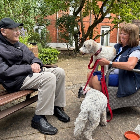 An older gentleman sat in a garden with a woman and her dogs