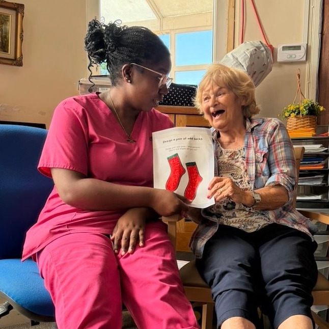 A resident and staff member sat together smiling holding a piece of paper