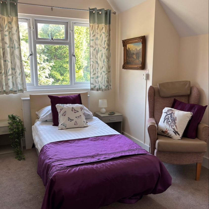A bright and airy bedroom with a comfortable single bed with purple bedding and armchair in front of the window