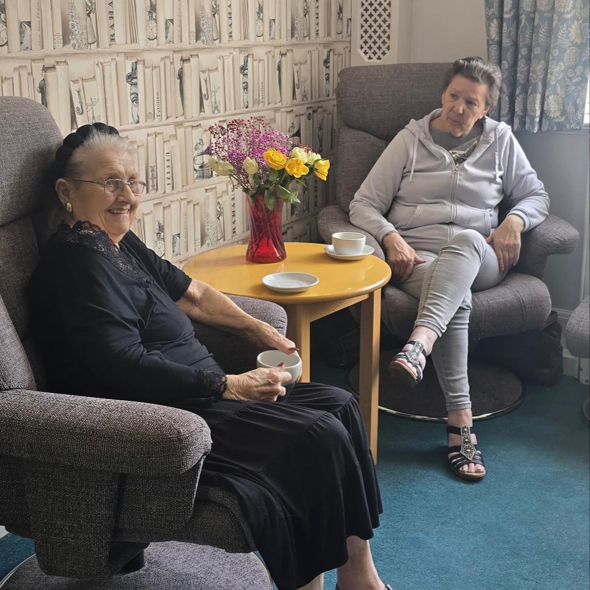 Two older women sat in armchairs smiling