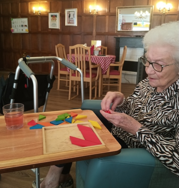 An older woman doing a puzzle game on a table