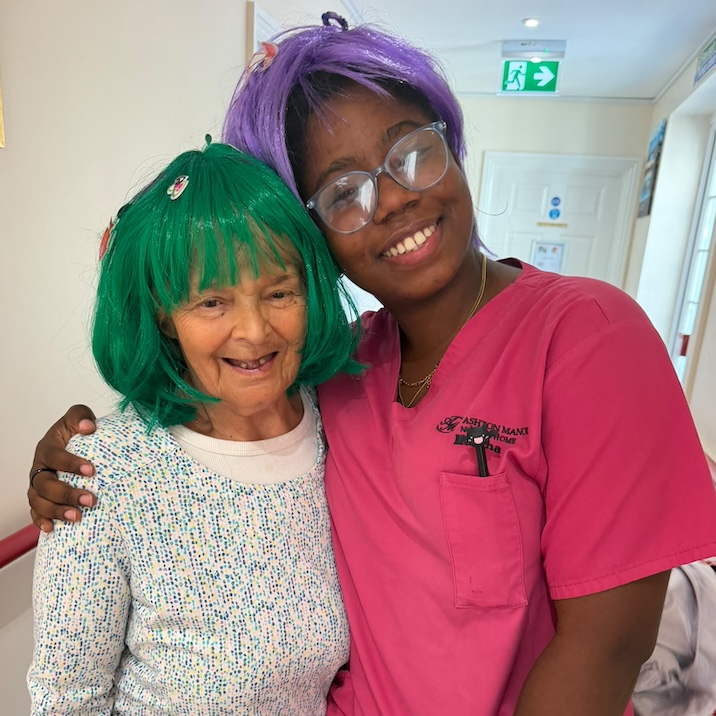An older woman and staff member wearing colourful wigs