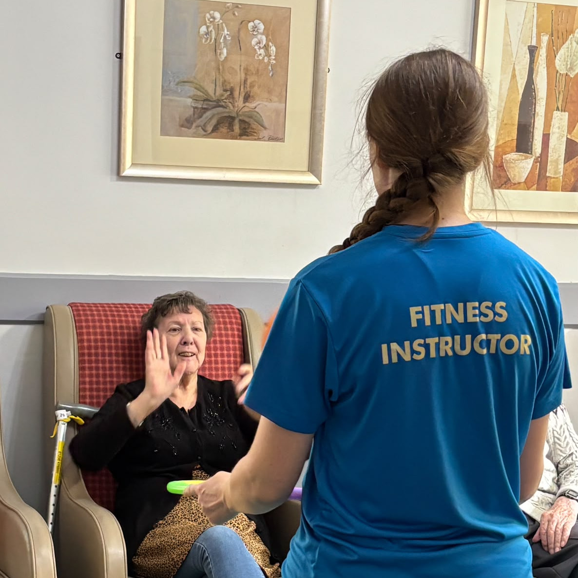 An older woman doing armchair exercises lead by an instructor