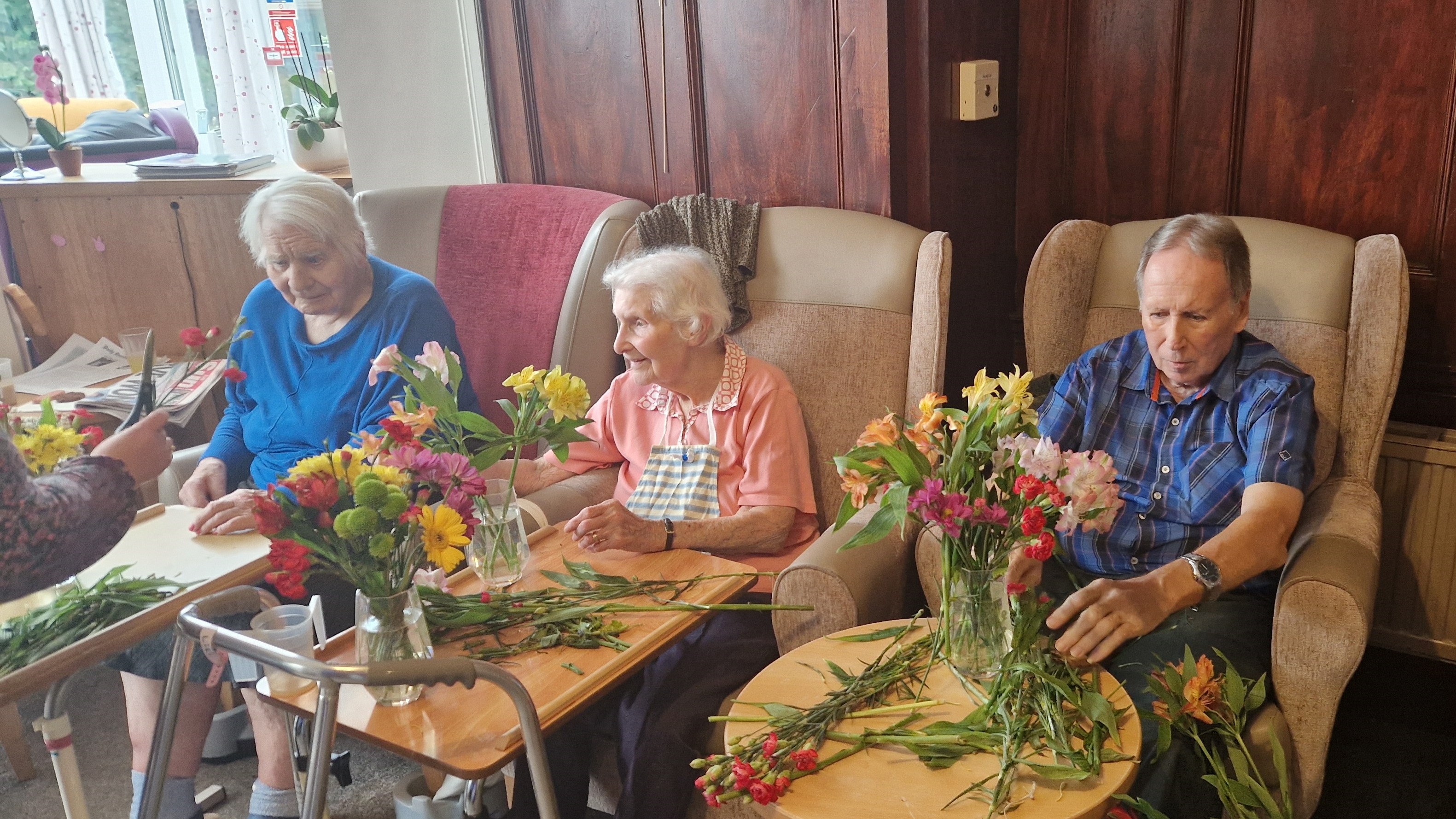 Three women arranging fresh flowers sat in arm chairs. 