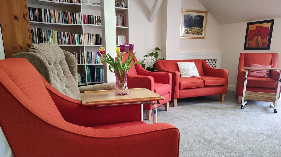 Five comfortable chairs arranged in front of a full bookshelf. There is a small table with fresh flowers on display.