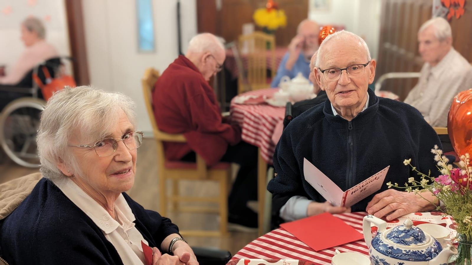 Three people sat in comfortable chairs. They are smiling and appear to be clapping along to something. 