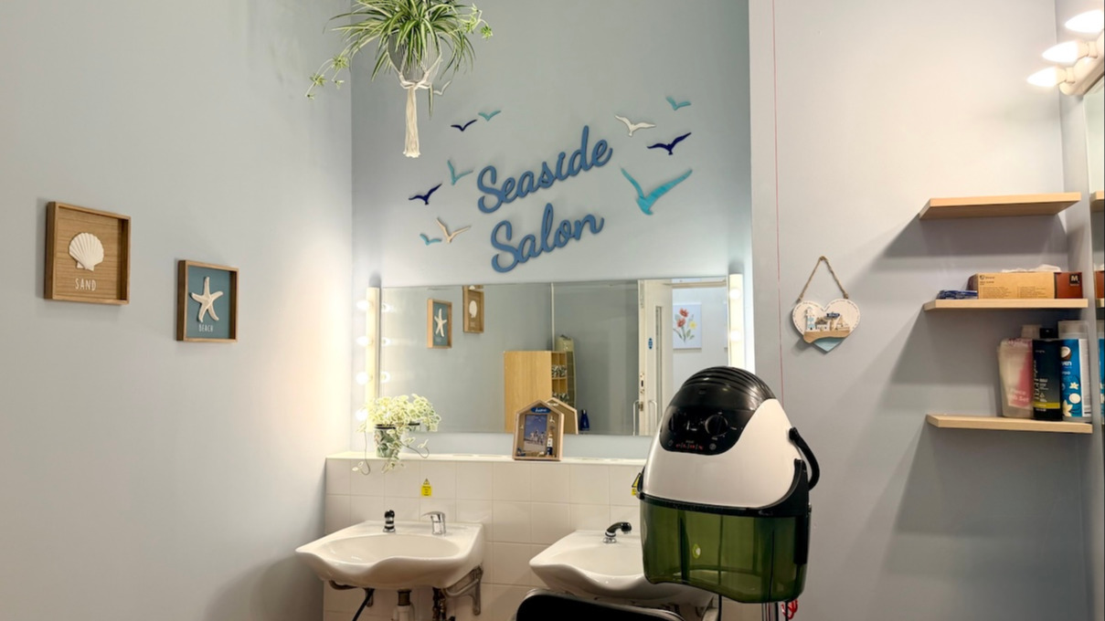 A clean salon with two sinks for washing hair a curling station. There are mirrors on the wall and the room is brightly decorated. 