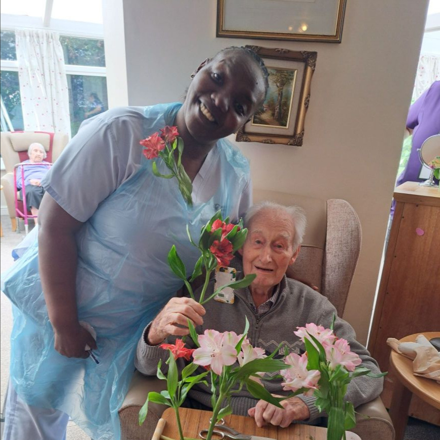 A smiling person with an elderly person with flowers