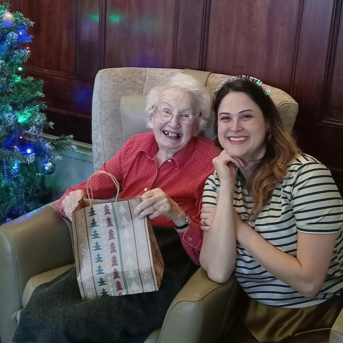 A smiling person with an elderly person with a gift at Christmas