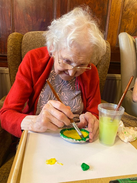 An elderly woman painting a small saucer