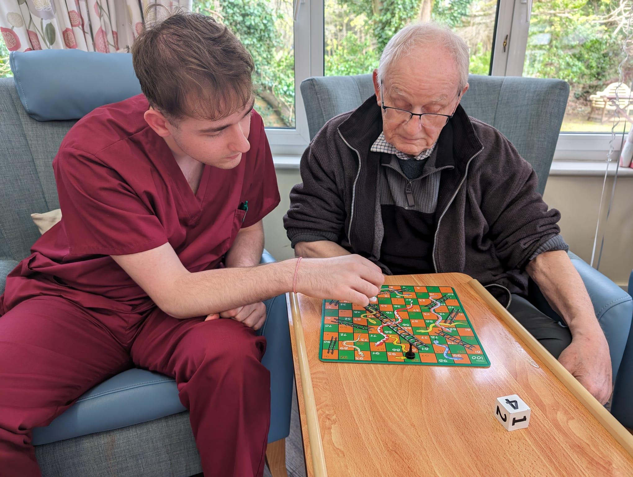 A care assistant and elderly man playing snakes and ladders