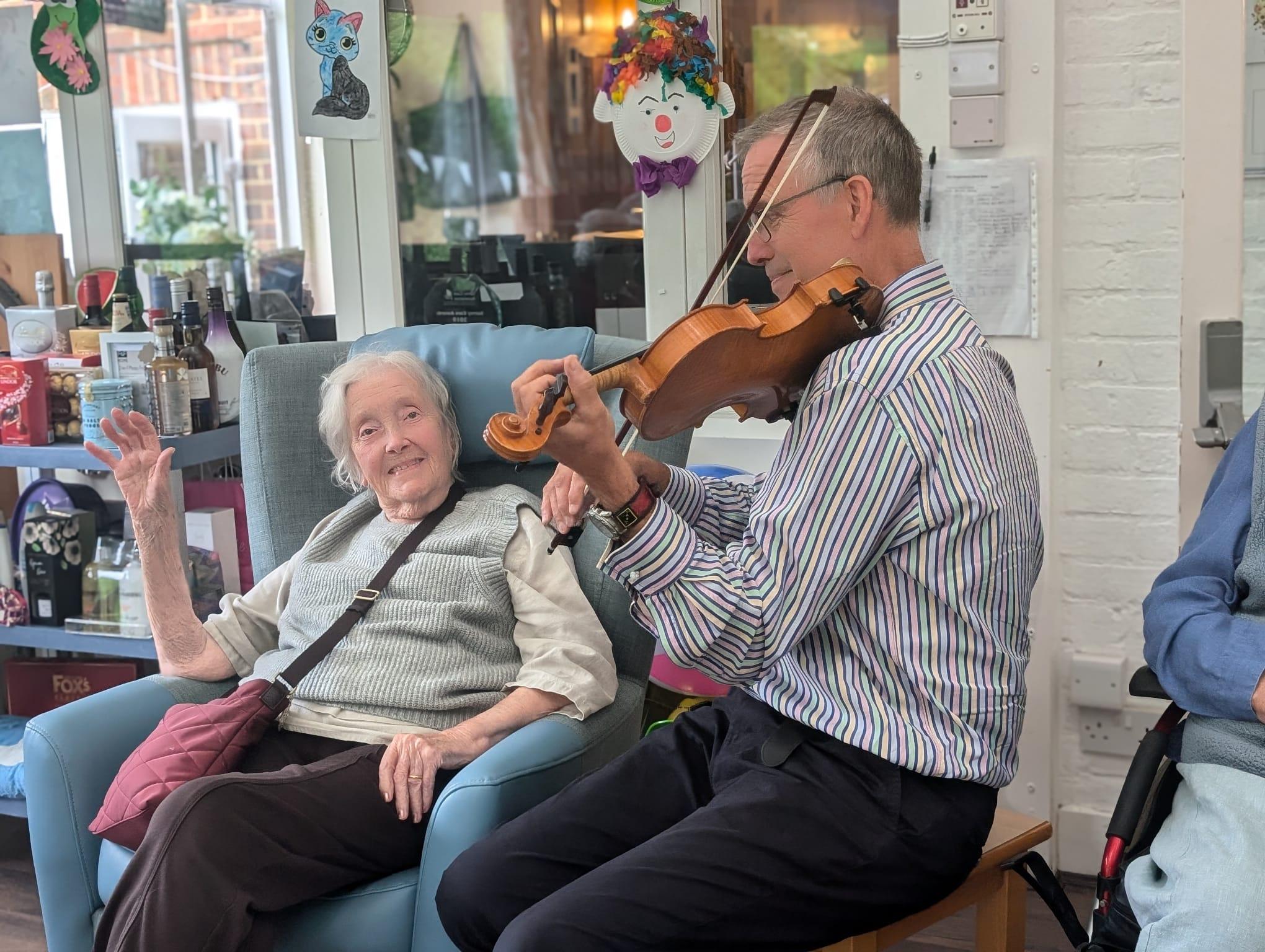 An elderly woman enjoing a violist play sat next to her