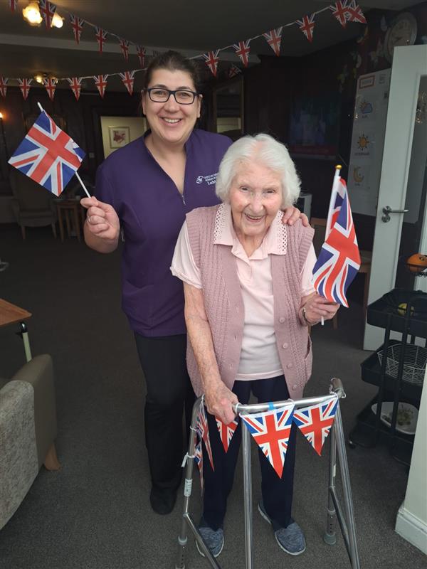 A staff member and elderly lady smiling and waving flags