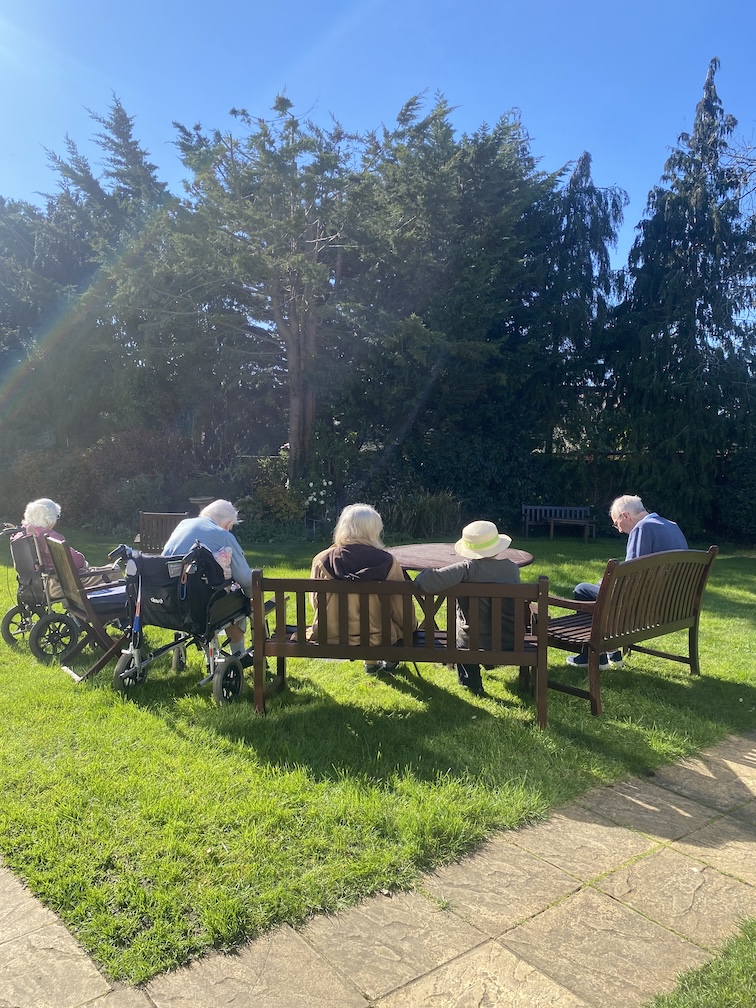 A group of elderly people sat on a garden bench in a sunny garden