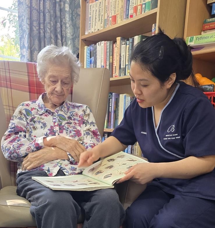 A staff member an elderly woman reading a book