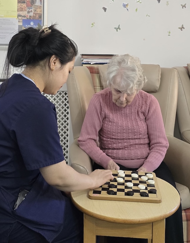 A staff member an elderly woman reading a book