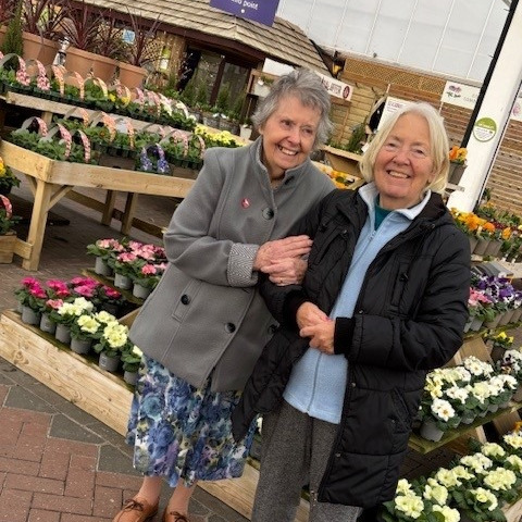 Two older women stood in front of a display of flowers at a garden centre