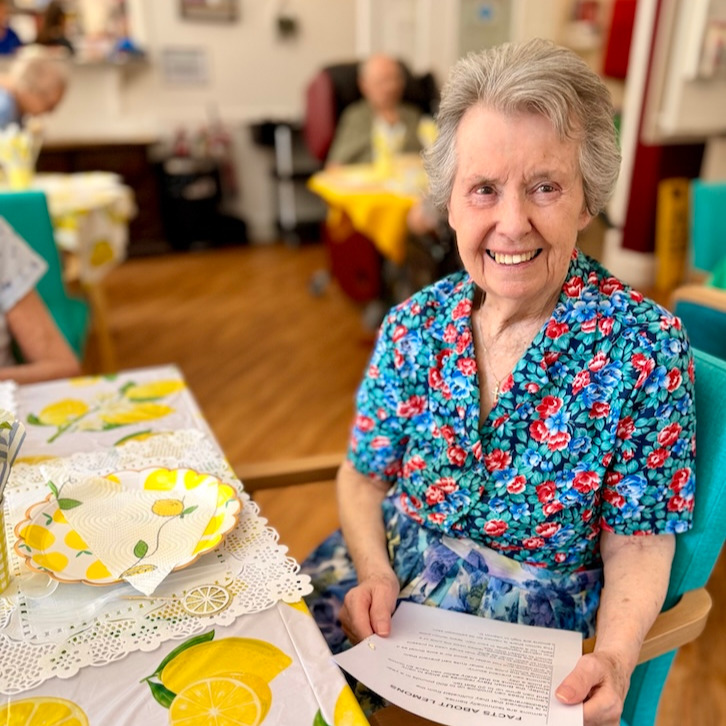 A woman smiling sat at a table holding a piece of paper